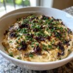 A close-up of a creamy caramelized onion dip topped generously with dark caramelized onions and fresh chopped chives.