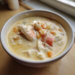 A close-up of a white bowl filled with rich, creamy crab soup featuring large chunks of white and orange crab meat.