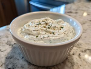 A close-up of a white ramekin filled with thick, creamy horseradish sauce, garnished with herbs.