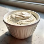 A small white ramekin filled with thick, creamy horseradish sauce speckled with black pepper.