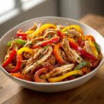 A white bowl filled with shredded chicken mixed with colorful sliced bell peppers for crockpot chicken fajitas.