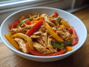 A white bowl filled with shredded chicken and colorful bell pepper strips, ready for crockpot chicken fajitas.