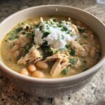 Close-up of a hearty bowl of crockpot white chicken chili topped with sour cream and fresh cilantro.