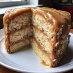 Close-up of a slice cut from a multi-layered caramel cake, showing thick caramel filling and topping.