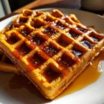 Close-up of golden brown pumpkin waffles generously topped with glistening syrup and a sprinkle of sugar.