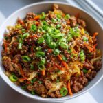 A close-up overhead shot of a hearty serving of egg roll in a bowl, topped with green onions and sesame seeds.