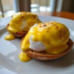 Two servings of Eggs Benedict topped generously with bright yellow hollandaise sauce and paprika.