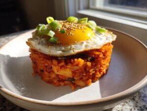 A molded serving of vibrant orange kimchi fried rice topped with a sunny-side-up egg, sesame seeds, and green onions.