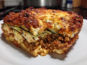 Close-up of a hearty serving of zucchini lasagna showing layers of meat sauce, ricotta, and browned cheese topping.