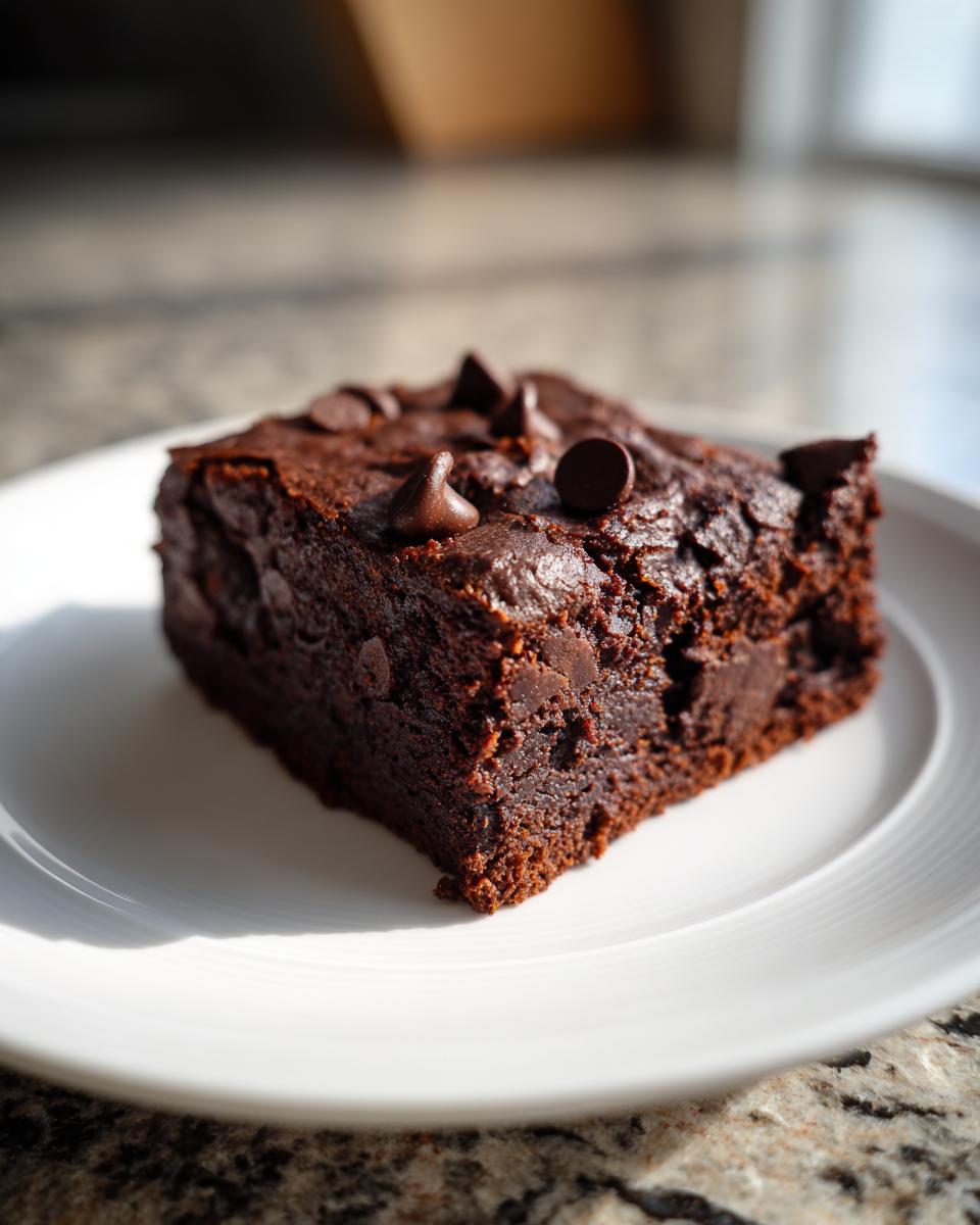 A single, fudgy square of sweet potato brownies topped with chocolate chips, served on a white plate.