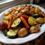 A white platter filled with glistening Garlic Herb Roasted Veggies, including potatoes, carrots, and zucchini slices.