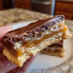 A hand holding half a delicious twix cookies bar showing layers of shortbread, caramel, and chocolate topping.