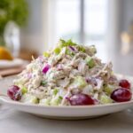 A mound of creamy greek yogurt chicken salad mixed with red onion and celery, garnished with grapes.