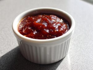 Close-up of thick, dark red homemade bbq sauce served in a small white fluted ramekin.