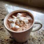 Close-up of a steaming mug of homemade hot cocoa topped generously with fluffy white marshmallows.