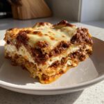 A thick, golden-brown slice of homemade lasagna with rich meat sauce and creamy cheese layers, sitting on a white plate.