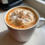 Close-up of a creamy pumpkin spice latte topped with whipped cream and cinnamon in a white mug.