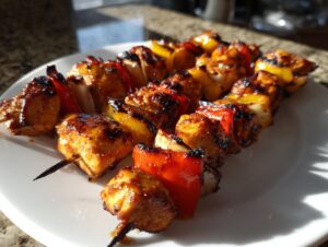 Close-up of three glazed honey garlic chicken skewers with charred edges and colorful bell peppers on a white plate.