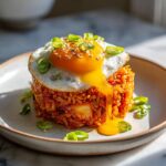 A molded serving of vibrant kimchi fried rice topped with a sunny-side-up egg, featuring a runny yolk dripping down the side.