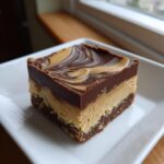 A single, thick square of no bake peanut butter bars showing three distinct layers and a chocolate peanut butter swirl topping.