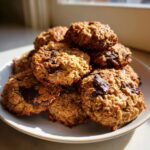 A stack of golden brown, oatmeal breakfast cookie treats loaded with melted chocolate chunks on a white plate.