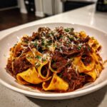 A close-up of wide pappardelle pasta generously coated in rich beef ragu, topped with grated Parmesan cheese and fresh parsley.