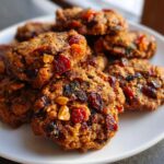 A stack of delicious, chewy fruitcake cookies loaded with dried cranberries and nuts, presented on a white plate.