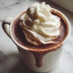 Close-up of a mug filled with rich, dark hot chocolate topped high with whipped cream, dripping down the side.