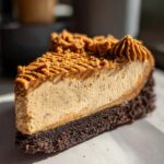 A rich, creamy slice of biscoff cheesecake featuring a dark chocolate crust and topped with Biscoff spread and crumbs.