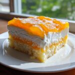 A square slice of Creamsicle Cake featuring layers of light sponge, white cream, and bright orange gelatin topping.