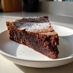 A decadent slice of flourless chocolate torte dusted with powdered sugar, served on a white plate.