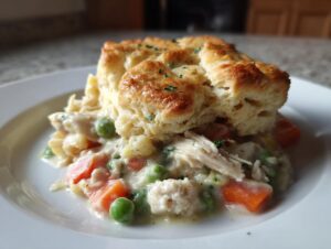 A serving of creamy slow cooker chicken pot pie topped with a golden biscuit on a white plate.