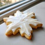 A close-up of a baked, snowflake-shaped sugar cookie topped with thick, white sugar cookie icing recipe.