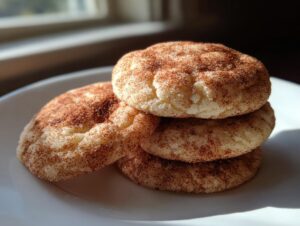A stack of three soft, chewy snickerdoodles coated in cinnamon sugar resting on a white plate.