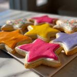 Close-up of star-shaped sugar cookies decorated with brightly colored sugar cookie icing that hardens, including pink, yellow, and orange.