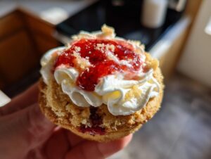 A hand holding one perfectly baked strawberry cheesecake cookies topped with whipped cream and strawberry jam.
