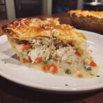 A close-up slice of turkey pot pie recipe showing shredded turkey, carrots, and peas in a creamy sauce under a golden, flaky crust.