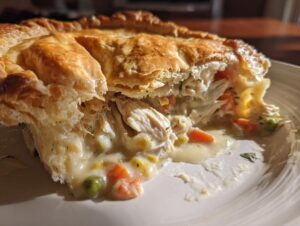 Close-up of a slice of turkey pot pie recipe showing flaky, golden crust and creamy filling with turkey and vegetables.