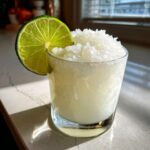 A frosty white Christmas margarita served in a rocks glass, topped with crushed ice and garnished with a bright lime wheel.