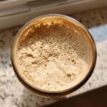 Overhead view of the bubbly, active sourdough starter in a glass jar, showing signs of fermentation.