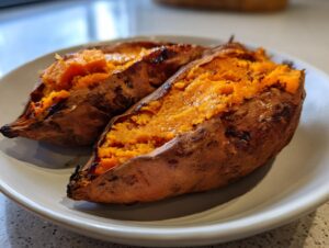 Two halves of a perfectly baked sweet potato showing fluffy, bright orange interior on a light plate.