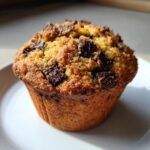A close-up of a perfectly baked banana chocolate chip muffin with a golden brown top studded with dark chocolate chunks.