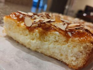 Close-up of a slice of bee sting cake showing thick vanilla cream filling, sponge cake, and caramelized almond topping.