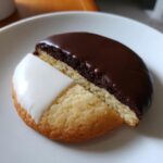 A close-up of a single black and white cookie, half covered in dark chocolate icing and half in white vanilla icing.