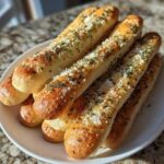 A close-up of several golden-brown, buttery breadsticks topped with grated Parmesan cheese and dried parsley.