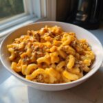 A close-up of a white bowl filled with creamy, cheesy cheeseburger pasta mixed with ground beef.