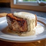 A thick, golden-brown chicken fried steak smothered in creamy, speckled country gravy on a white plate.