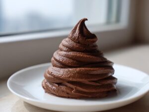 A tall, perfectly piped swirl of rich, dark chocolate buttercream frosting sitting on a small white plate.