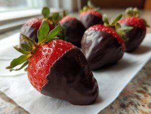 Close-up of several glossy chocolate covered strawberries with bright green tops resting on white parchment paper.