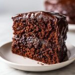 Close-up of a rich, moist slice of chocolate zucchini cake topped with glossy dark chocolate frosting.
